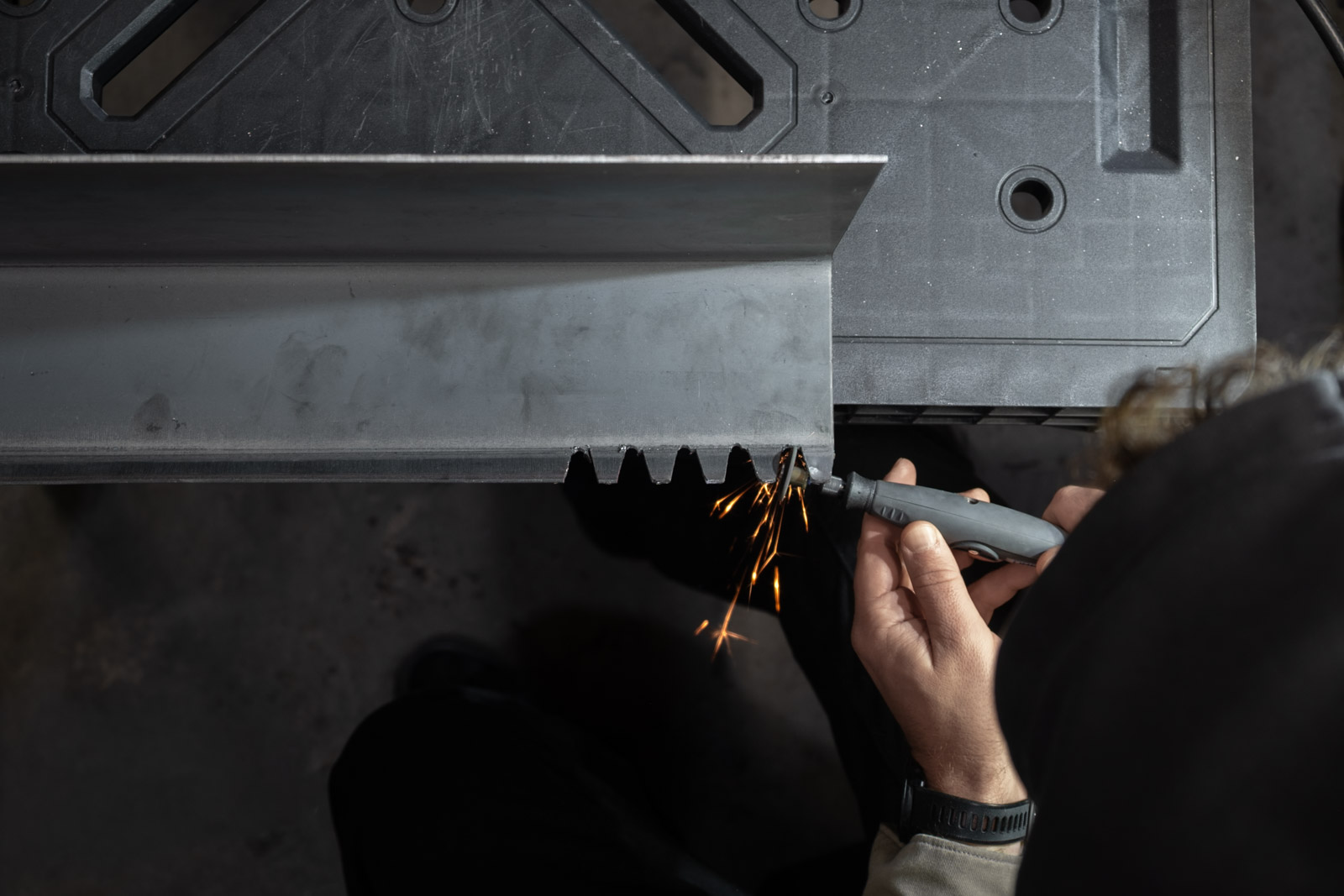 Fabrication process showing a person using a rotary tool to cut key notches into a raw steel BND Series entryway shelf.